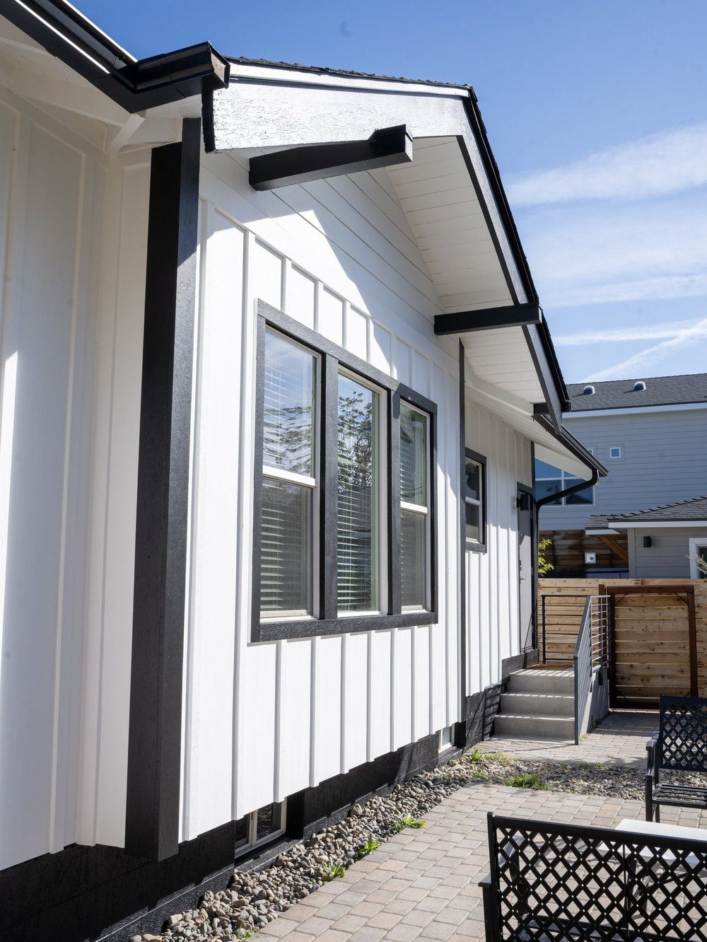 Side view of a finished Renovations INC project — white board-and-batten siding with black trim, multi-pane vinyl windows, and a paver patio in Sparks, NV