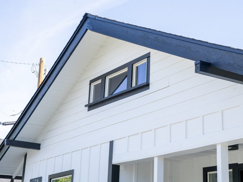 Black-frame replacement windows on a white board-and-batten gable — Renovations INC project